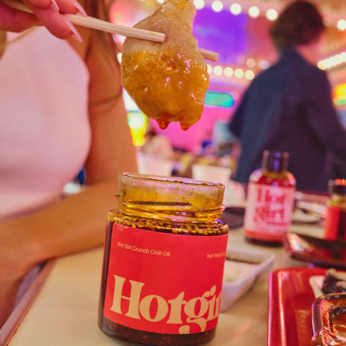 Person holding a dumpling over a jar of Hotgirlsauce chili oil hot sauce with a blurred background.