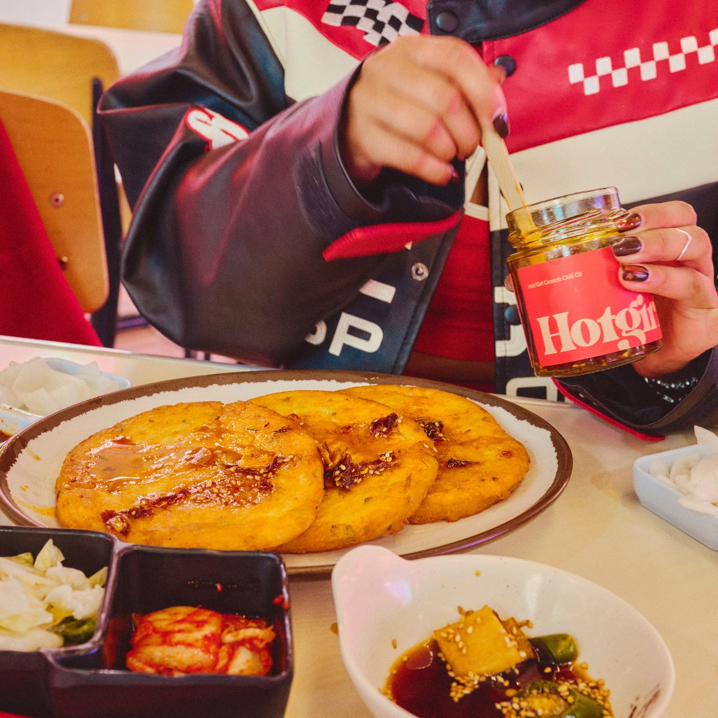 Person eating at a table with a plate of food and a jar of hot sauce chili oil.