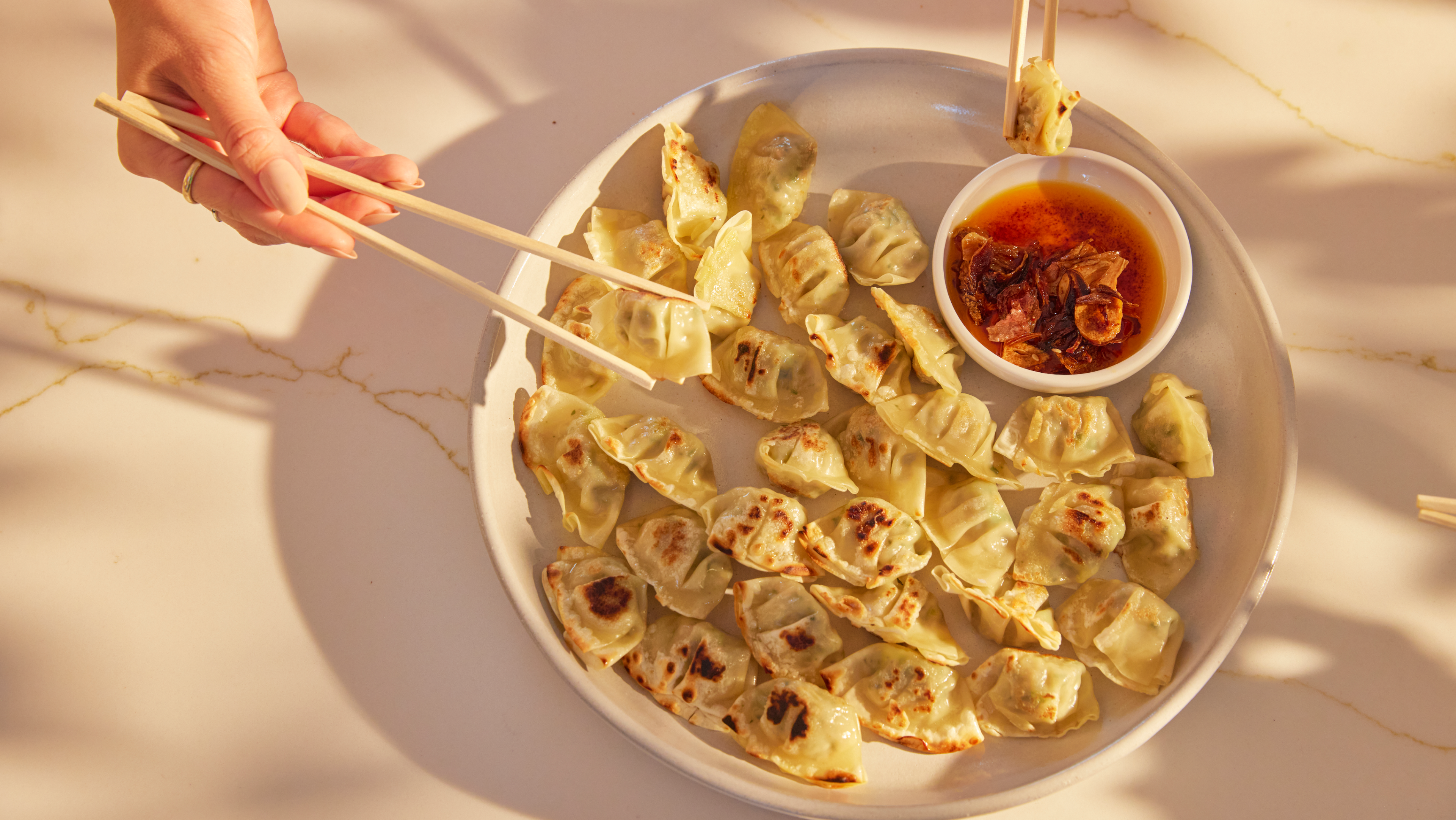Friends reaching for dumplings off a platter and dipping into a saucer of vibrant, silky smooth Hot Girl Crunch Chili Oil with crispy chili crunches - Hotgirlsauce chili oil - chili sauce - hot sauce