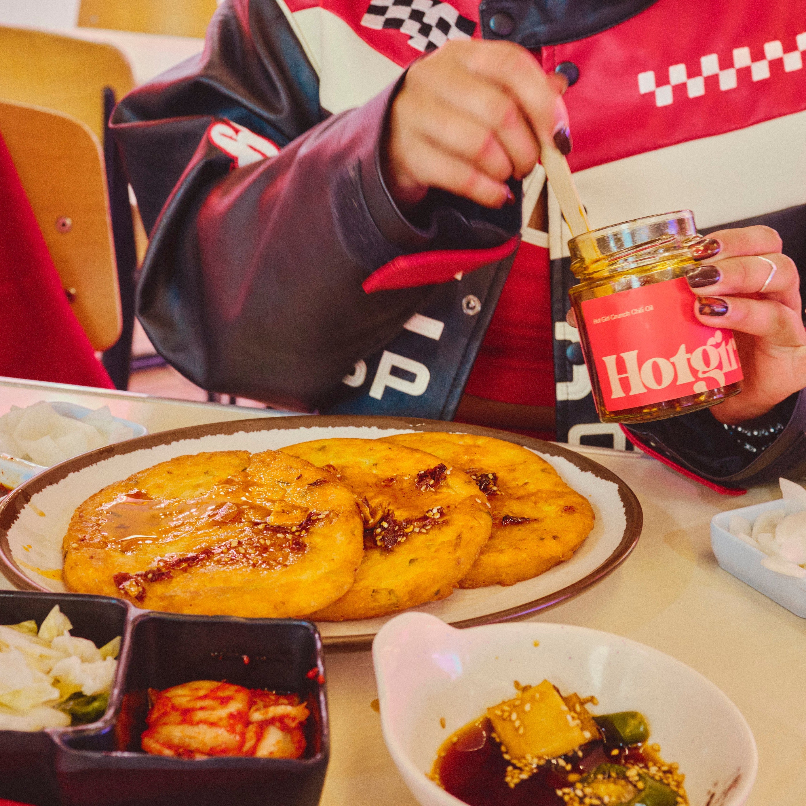 Person eating at a table with a plate of food and a jar of hot sauce chili oil.
