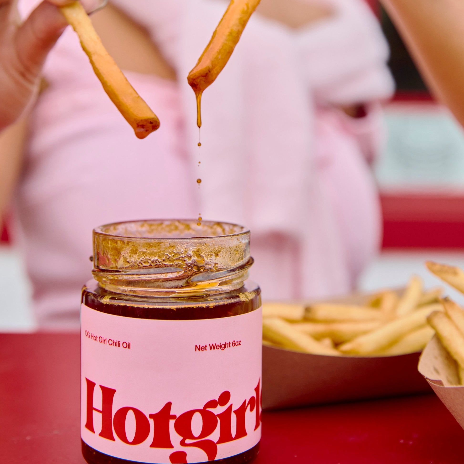 Person dipping a french fry into a jar of Hotgirlsauce chili oil hot sauce with another fry held above it.

